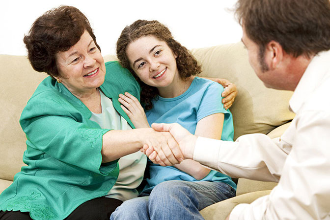 Elderly woman shaking hands with man sitting on couch